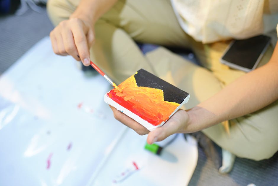 A person painting vibrant abstract art on a small canvas with red, orange, and black colors.
