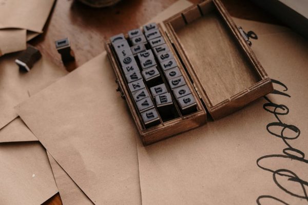Vintage wooden box containing rubber alphabet stamps on brown paper envelopes.