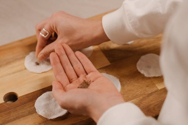 Hands creating seed bombs using cotton pads and seeds on a wooden surface, promoting eco-friendly gardening.
