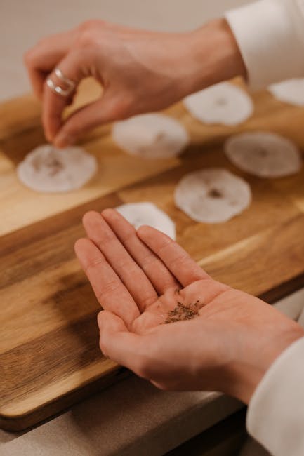 Hands sprinkling spices on food, showcasing culinary preparation in warm indoor setting.