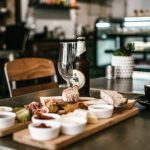 Rustic dining scene featuring craft beer, deli platter, and cappuccino in a cozy cafe atmosphere.