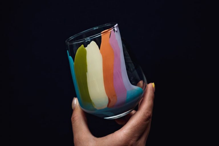 A close-up of a hand holding a glass with vibrant rainbow colors on a dark background.
